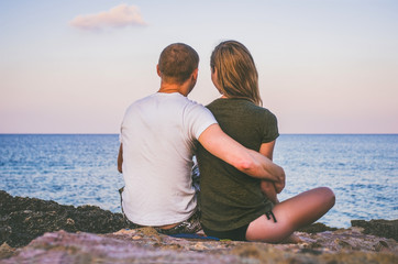 Man and woman hugging sitting on beach and watching the calm sea at sunset