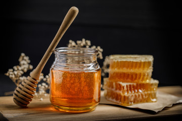 Honeycomb with honey dipper and dry flower on black background, bee products by organic natural ingredients concept