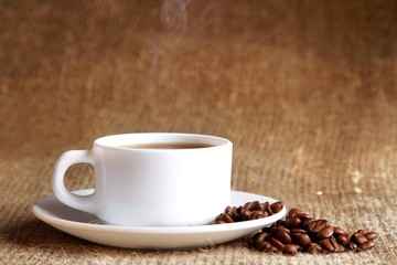 Sticker - Cup of hot coffee with beans on wooden background