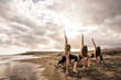 © simona - group of young beautiful caucasian women doing fitness exercises at the beach on the shore. blue ocean and sky in the background. enjoying sport outdoor leisure activity together in friendship or team