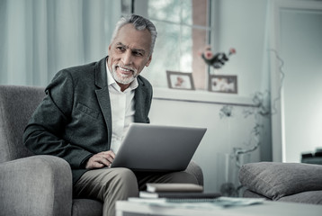 Wall Mural - Have idea. Handsome male keeping smile on his face, holding laptop on knees and looking aside