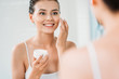 © LIGHTFIELD STUDIOS - beautiful smiling young woman applying face cream and looking at mirror