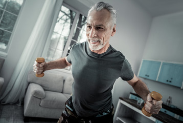 Wall Mural - Strong will. Delighted gray-haired man keeping smile on his face while being at home