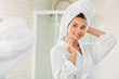 © LIGHTFIELD STUDIOS - beautiful smiling young woman in bathrobe and towel on head looking at mirror in bathroom