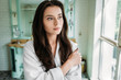 © LIGHTFIELD STUDIOS - pensive brunette girl in bathrobe looking at window in bathroom