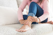 Closeup woman sitting on sofa holds her ankle injury, feeling pain. Health care and medical concept.