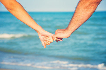 A man holds a woman by the hand on the beach by the sea, the concept of family, love and peaceful life.