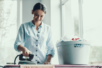 Young Smiling Woman Ironing Clothes after Laundry