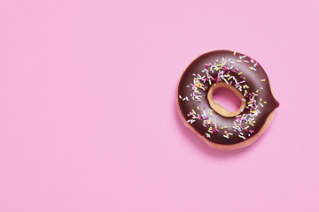 Single classic chocolate ring donut (doughnut) with sprinkles on a pastel pink background with space for copy