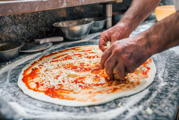 Chef spreading cheese on pizza base. Close-up.