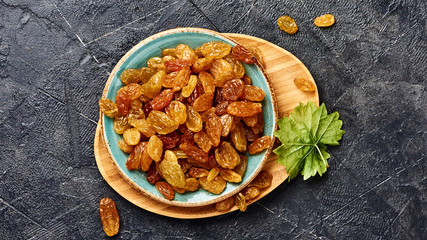 Wall Mural - Yellow big raisins on black concrete background with copy space. Top view of dried grapes.