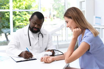 Wall Mural - Young African-American doctor checking patient's blood pressure in hospital