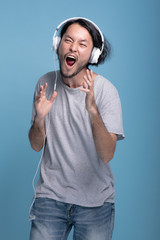 Young bearded man listening to music in blue background.