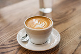 Latte art in cappuccino coffee cup at cafe table. Closeup of rosetta flower drawing in foam.