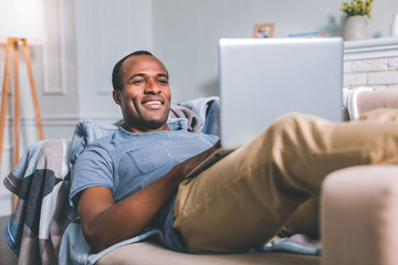 Freelance. Relaxed high-spirited man laying in the sofa while working at home