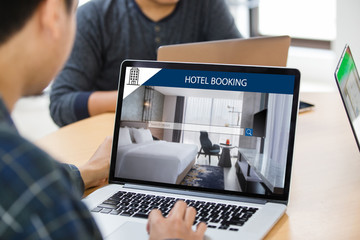 Man working on laptop, searching for lodging using on-line web service, booking a hotel on website at office