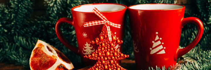 Close-up two glass cups full of hot, red, aromatic lemon tea with dark chocolate on a pine branch and table background. Winter snacks composition.