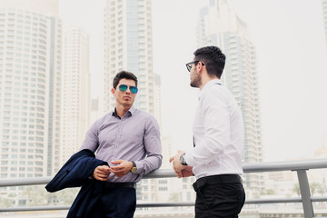 Wall Mural - Two young modern businessman in Dubai Marine leaned on fence. Standing and discussing about business.