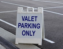 A White And Blue Valet Parking Sign In The Parking Lot.