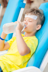 Little boy on the beach with a sunstroke drink water