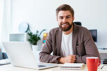 portrait of young startup businessman sitting in small modern office and looking at camera