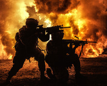 Silhouettes Of Two Army Soldiers, U.S. Marines Team In Action, Surrounded Fire And Smoke, Shooting With Assault Rifle And Machine Gun, Attacking Enemy With Suppressive Gunfire During Offensive Mission