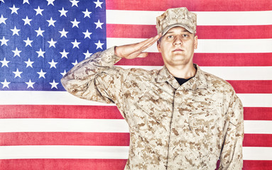 Wall Mural - Portrait of U.S. army soldier in camouflage uniform and cap saluting on background of flag of United States of America, looking at camera. Military hand salute to display respect for national flag