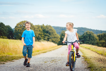 Poster - Junge und Mädchen laufen und fahren Fahrrad auf einem Feldweg