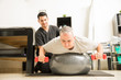 © AntonioDiaz - Patient Lifting Dumbbells While Lying On Exercise Ball By Physiotherapist