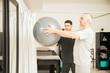 © AntonioDiaz - Physiotherapist Assisting Elderly Man Lifting Exercise Ball
