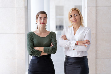 Business team of two young female professionals. Successful young business women posing with arms crossed. Teamwork concept