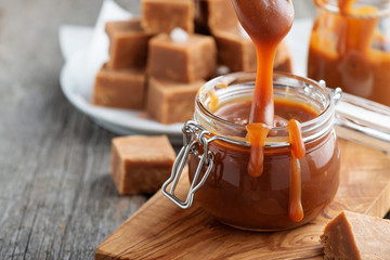 Homemade salted caramel sauce in jar on rustic wooden table.