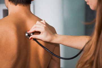 Female doctor examining patient with stethoscope at medical cabinet at clinic. Health care and physician concept