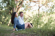 © soleg - young couple sitting on the grass in the forest and looking on sunset, summer nature, bright sunlight, shadows and green leaves, romantic feelings