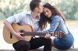 © soleg - young couple sitting on a log by the river and playing guitar, summer nature, bright sunlight, shadows and green leaves, romantic feelings