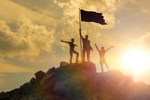 Silhouettes Of Happy Three People On Top Of A Mountain With The Flag Of Victory. Success And Achievements, Business, Work In A Team, Cooperation.