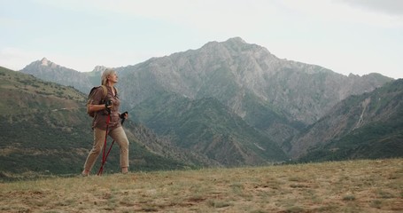 mature caucasian woman hiking in mountains with backpack, enjoying her adventure - tourism concept c