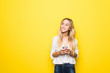 Portrait of a young woman using mobile phone isolated over yellow background