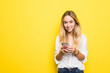 © F8  \ Suport Ukraine - Portrait of young girl holding mobile phone while standing isolated over yellow background