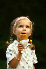 Wall Mural - Candid portrait of a girl in white shirt eating ice cream outdoor in the park. Blurred background