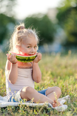 Wall Mural - Little blond girl eating watermelon in the park.