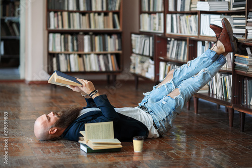 Cuadros en Lienzo Bearded hipster man relax and reading book lies on the floor