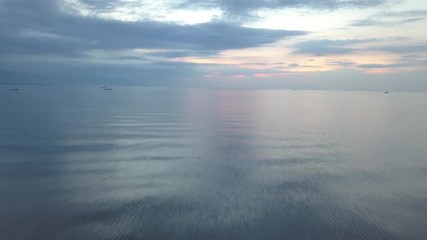 Wall Mural - moving backward over calm ocean water surface at sunset time with colorful cloudy background, aerial