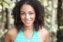 Beautiful African American Woman With Long Curly Hair, Green Eyes And Flawless Skin Wearing A Turquoise Dress Smiling In The Country Outside In The Sunlight