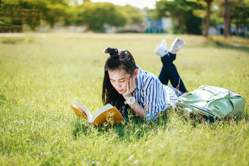 Asian woman  is reading a book on a green grass in the garden, She is preparing for the final exam this summer.