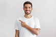 © Damir Khabirov - Handsome man in white t-shirt pointing left with finger isolated on gray background