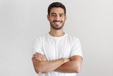 Fototapeta Do przedpokoju - Portrait of smiling handsome man in white t-shirt, standing with crossed arms isolated on gray background