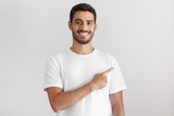 Fototapeta Do przedpokoju - Handsome young man in white t-shirt pointing right with his finger isolated on gray background