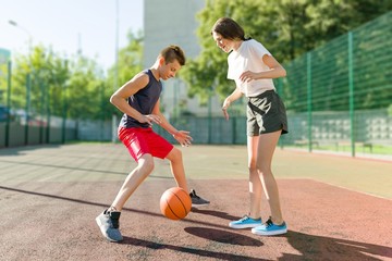 Streetball basketball game with two players, teenagers girl and boy, morning on basketball court