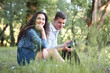 © soleg - young couple sitting on the grass in the forest and looking on sunset, listen to radio, summer nature, bright sunlight, shadows and green leaves, romantic feelings